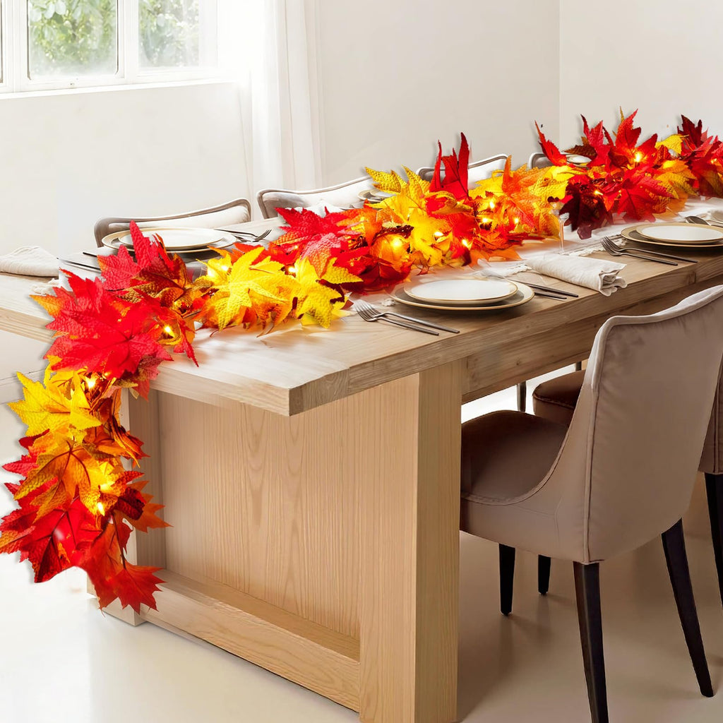 Fall maple leaf garland with warm orange lights draped across a dining table set for a meal.