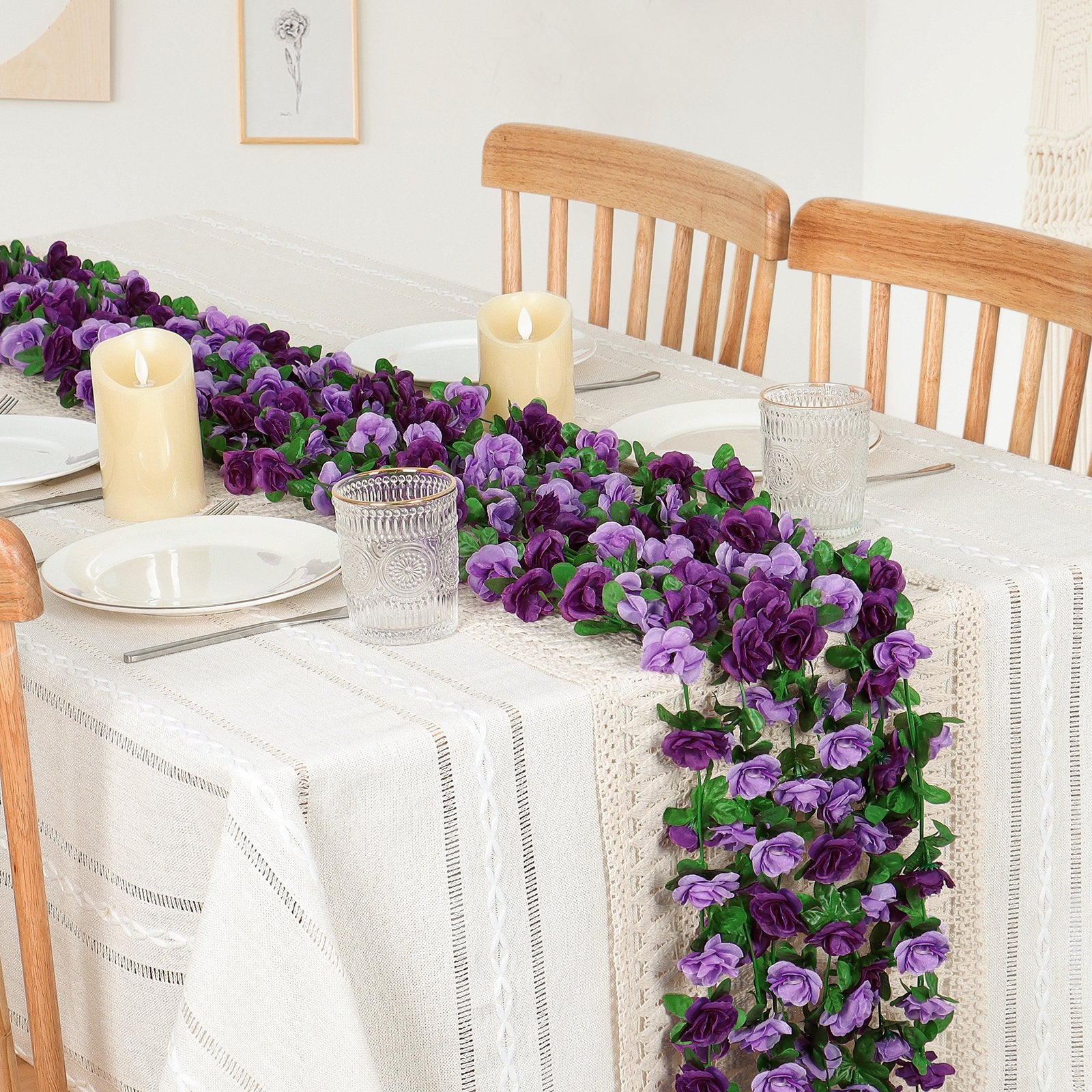 Artificial purple rose garland draped across a table setting with candles and plates.