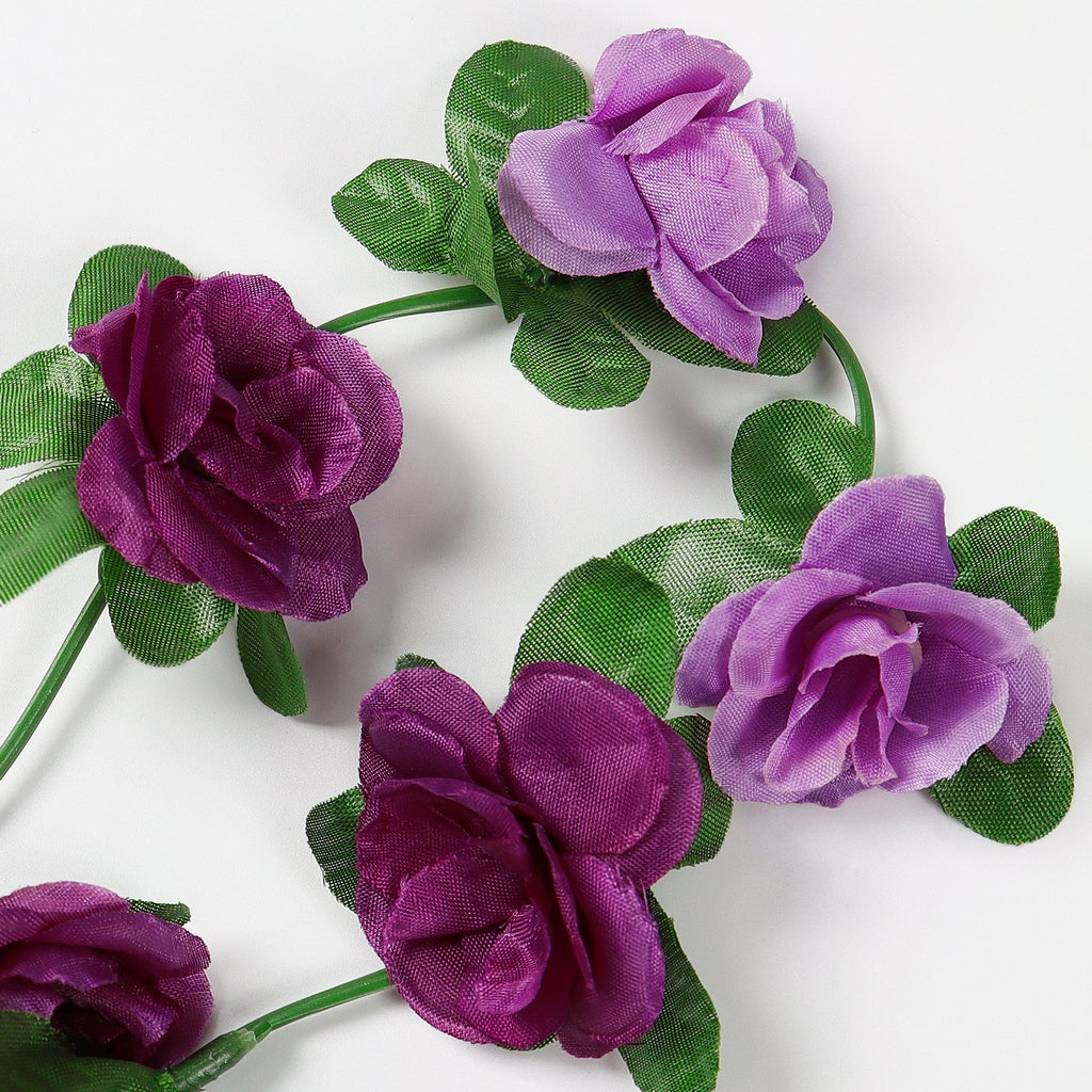 Artificial purple rose garland with green leaves on a white background, close-up view