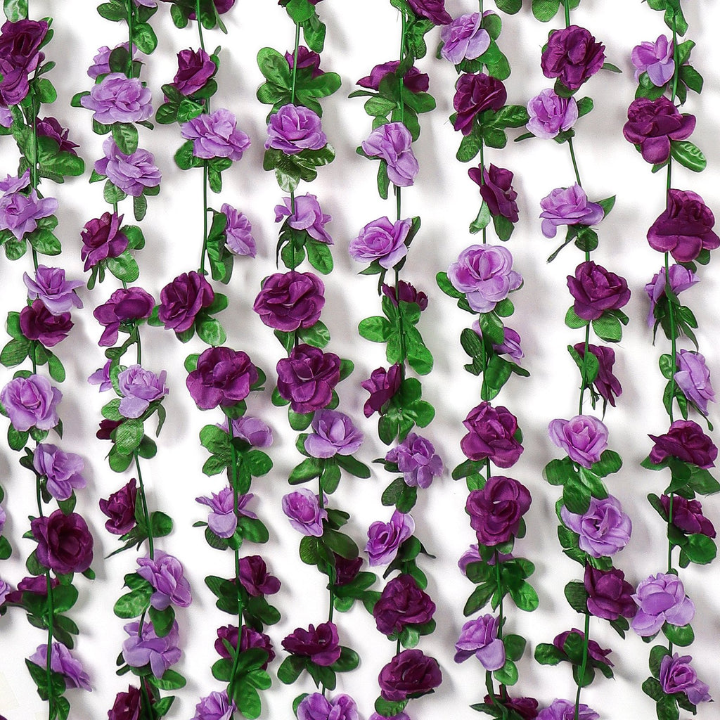 Multiple strands of artificial purple rose garlands with green leaves against a white background.