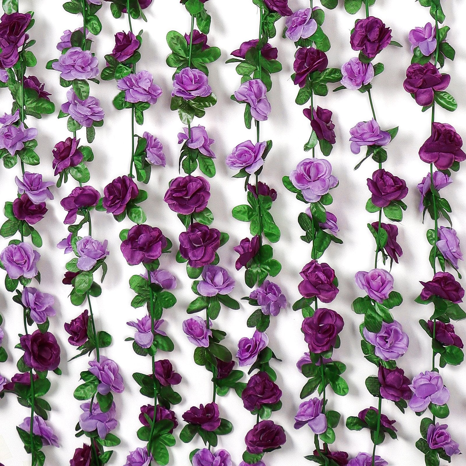 Multiple strands of artificial purple rose garlands with green leaves against a white background.