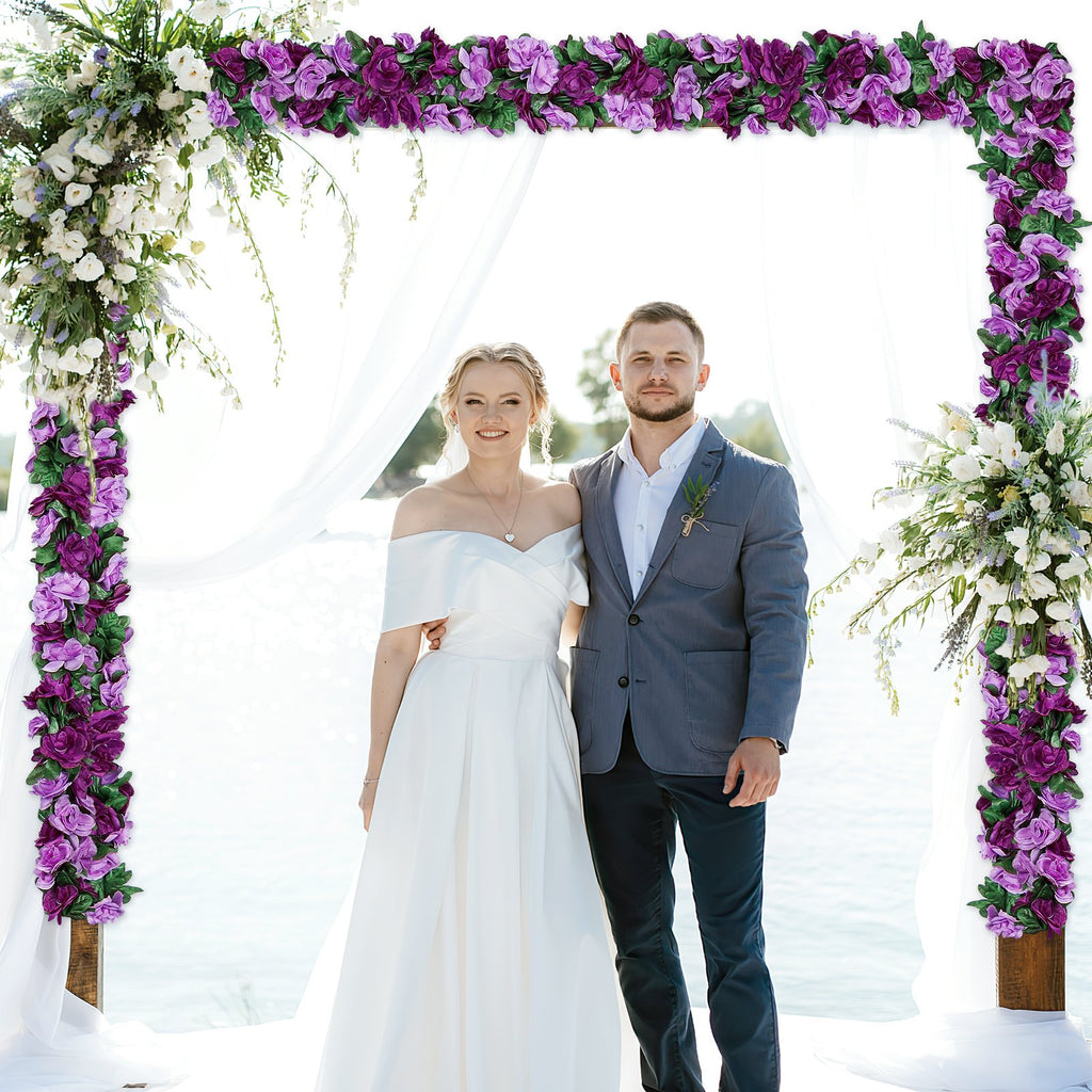 Bride and groom standing under a wedding arch decorated with purple and white flowers.