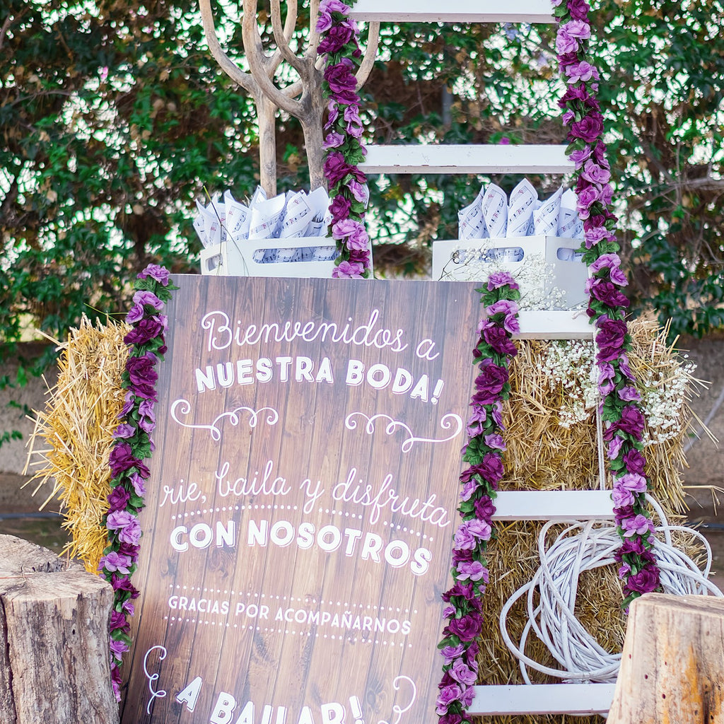 Wedding welcome sign with purple rose garlands and hay bales, decorated for a celebration.