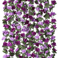 Artificial purple rose garland with green leaves hanging vertically against a white background.