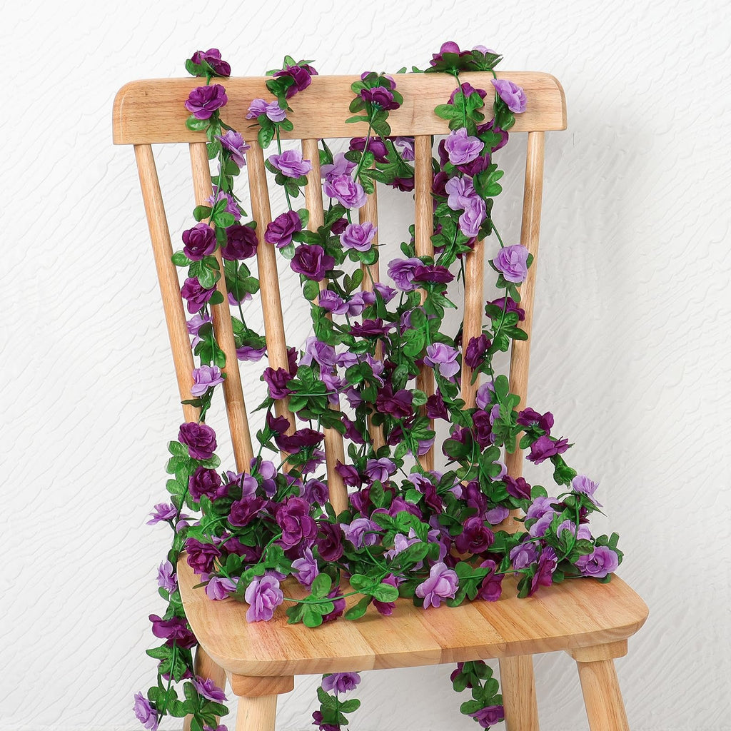 Artificial purple rose garland draped over a wooden chair, showcasing numerous flowers and green leaves.
