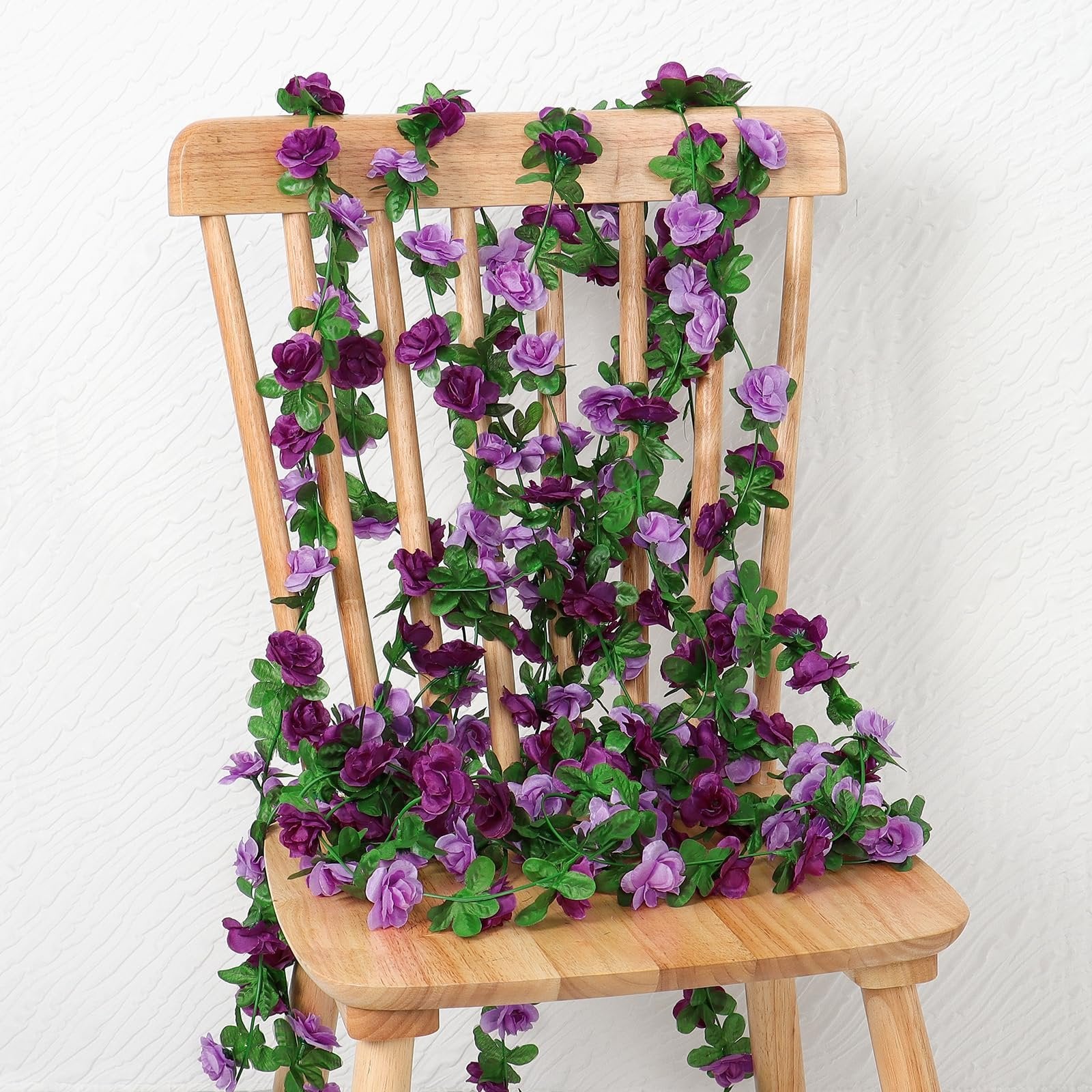 Artificial purple rose garland draped over a wooden chair, showcasing numerous flowers and green leaves.