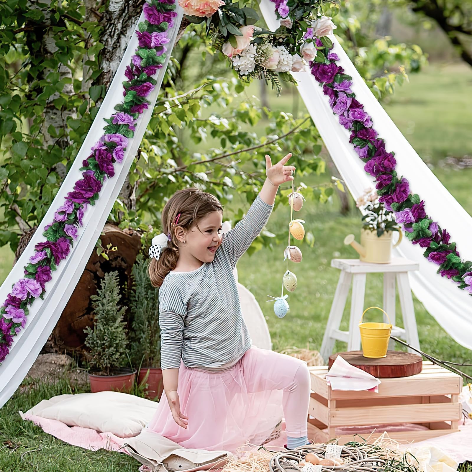 Young girl in a pink tutu holding Easter eggs under a floral arch decorated with purple rose garlands
