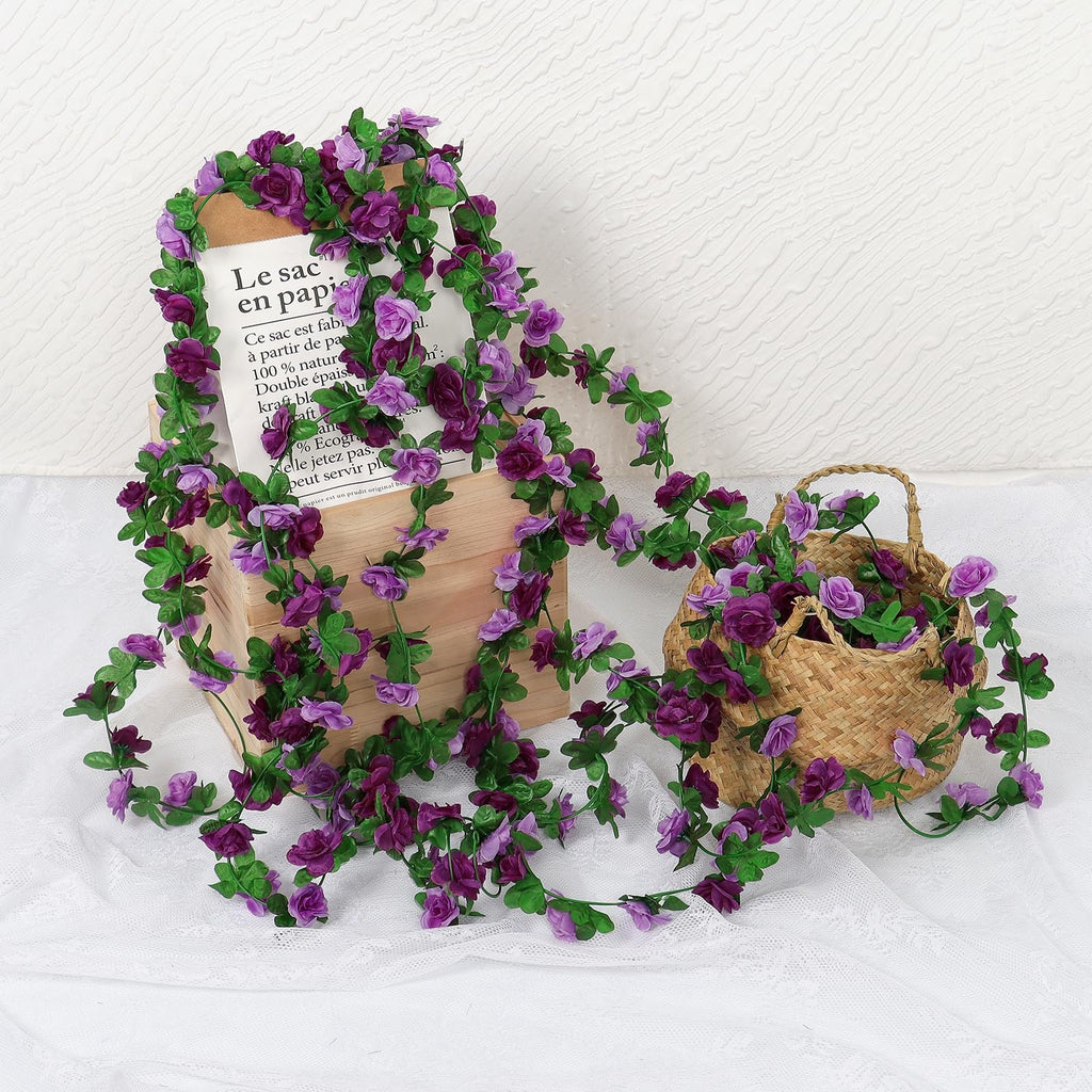 Artificial purple rose garland draped over a wooden box and spilling into a woven basket, with a paper bag visible.