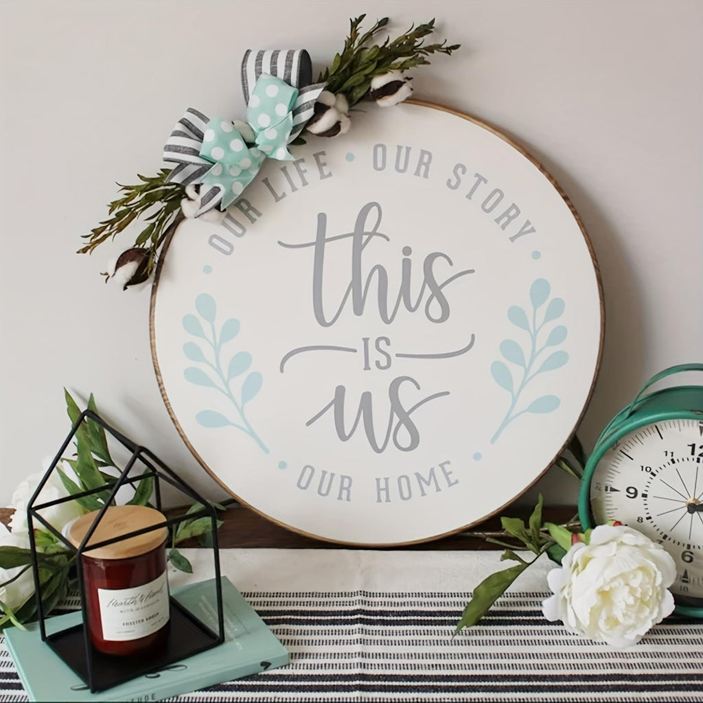 Round wooden sign with 'this IS us OUR HOME' text and floral accents, displayed with a candle and clock.