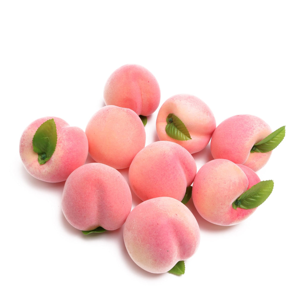Nine artificial pink peaches with green leaves scattered on a white background