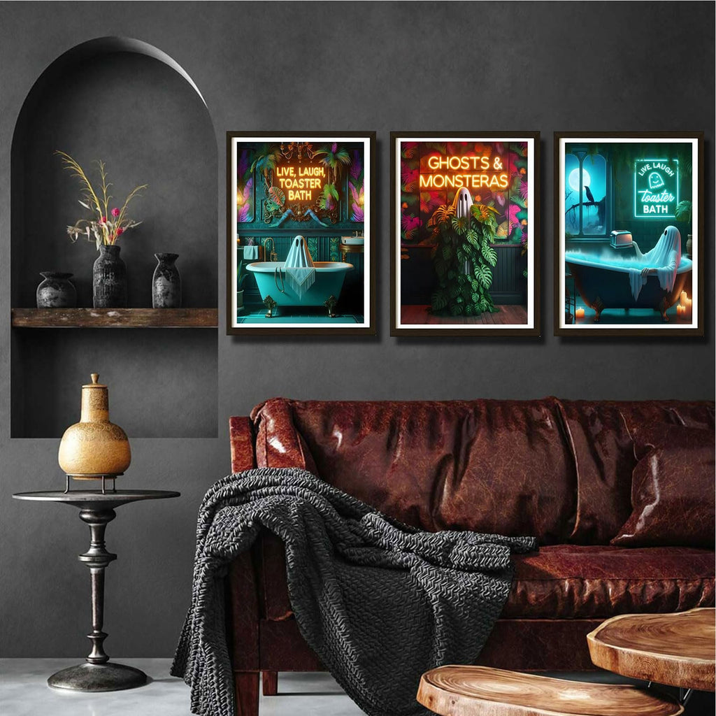 Three framed Halloween-themed art prints depicting ghosts in bathrooms and plants, displayed above a leather sofa.