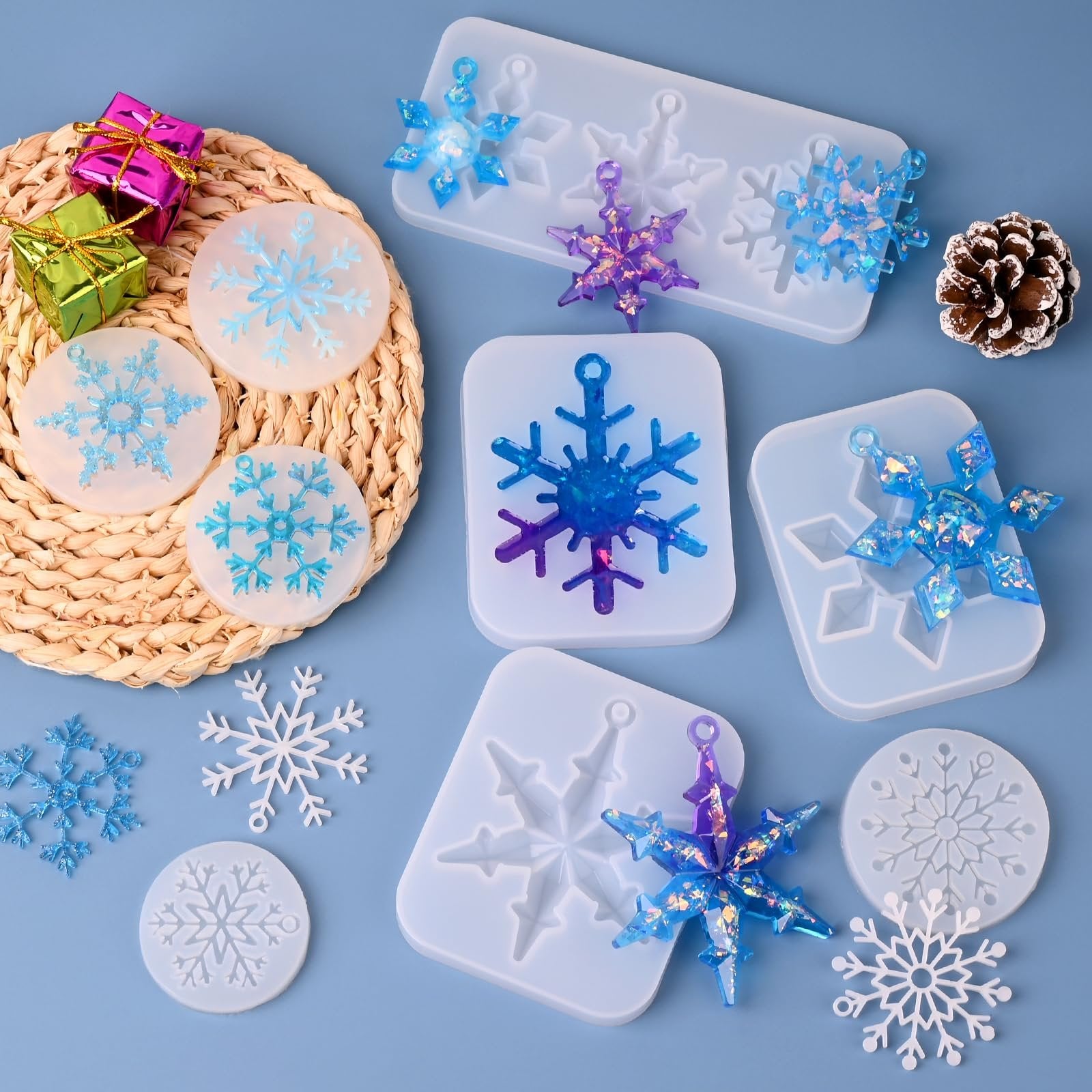 Silicone snowflake resin molds with finished snowflake ornaments, small gift boxes, and a pinecone on a blue background.