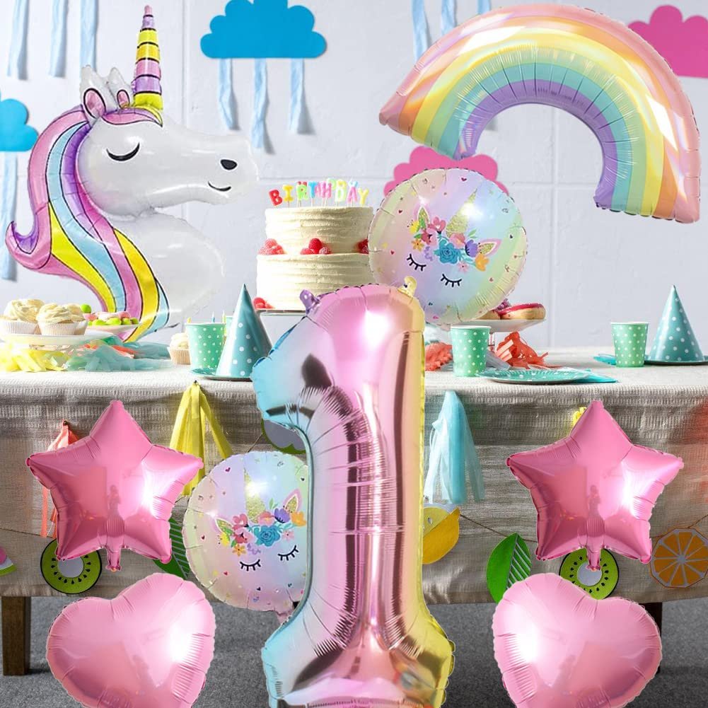 Unicorn and rainbow foil balloons arranged on a table with a birthday cake and party decorations.