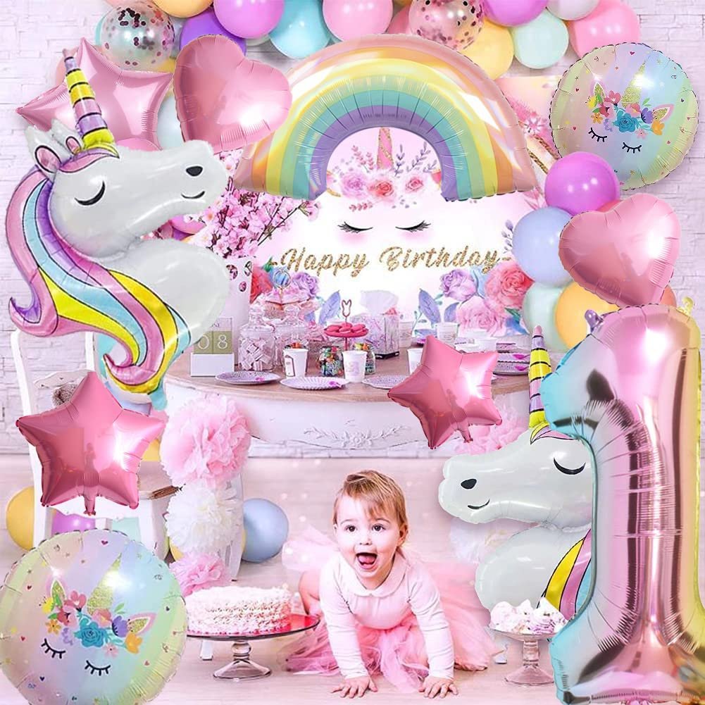 Birthday party scene with unicorn balloons, rainbow, number 1, stars, hearts, and a baby girl in a pink tutu.