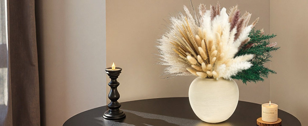 Arrangement of dried pampas grass and other botanicals in a textured vase, next to a black candlestick and a lit candle.