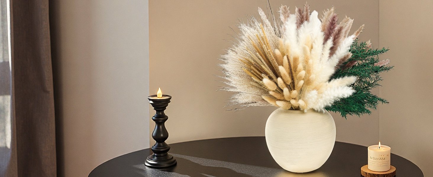 Arrangement of dried pampas grass and other botanicals in a textured vase, next to a black candlestick and a lit candle.