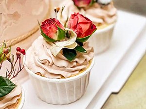 Close-up of three frosted cupcakes decorated with small red roses and greenery, presented on a white tray.