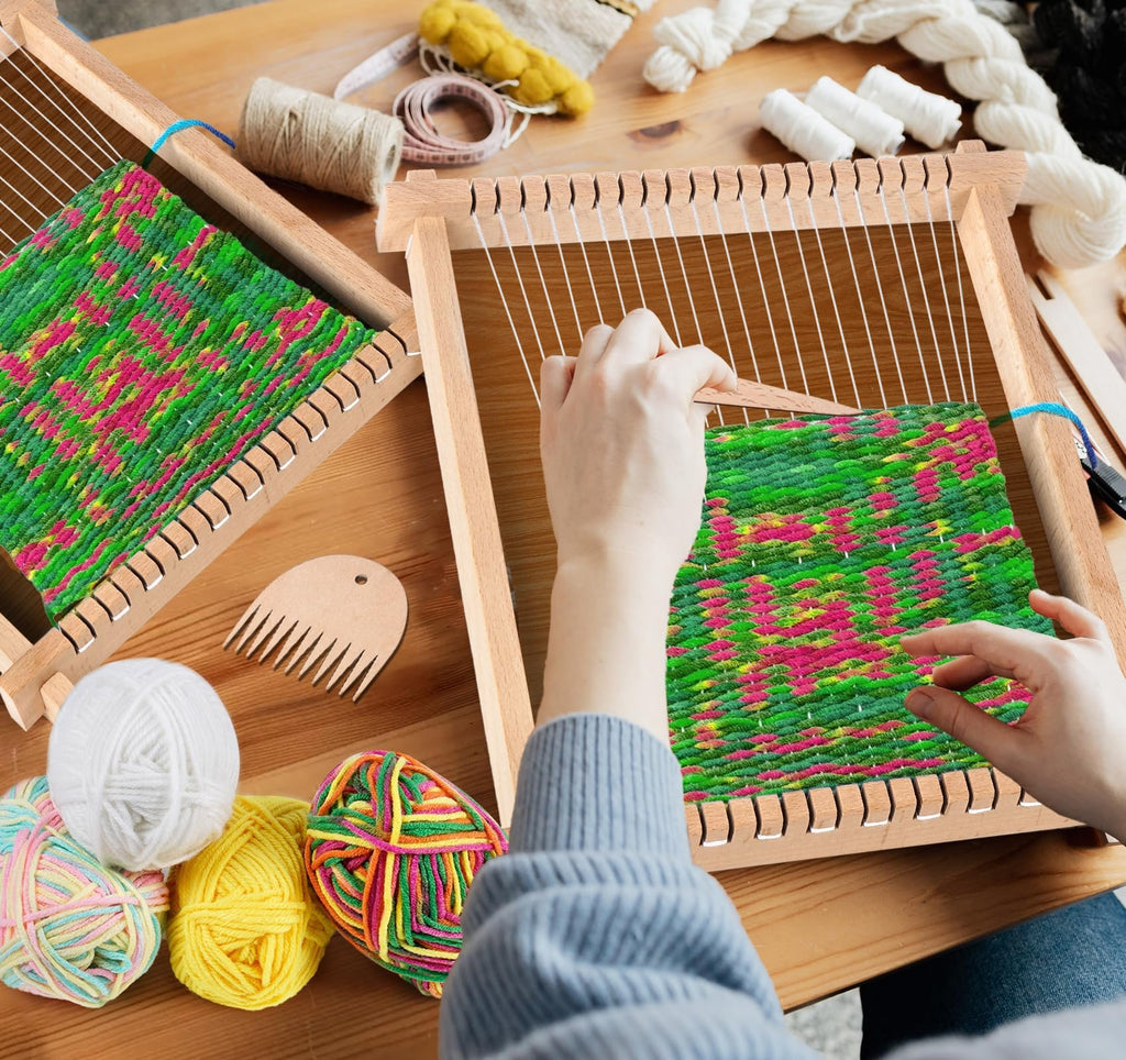 Hands weaving on a wooden loom kit with colorful yarn and tools on a wooden table.
