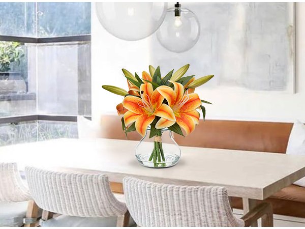 Orange tiger lily artificial flower arrangement in a glass vase with faux water on a dining table.