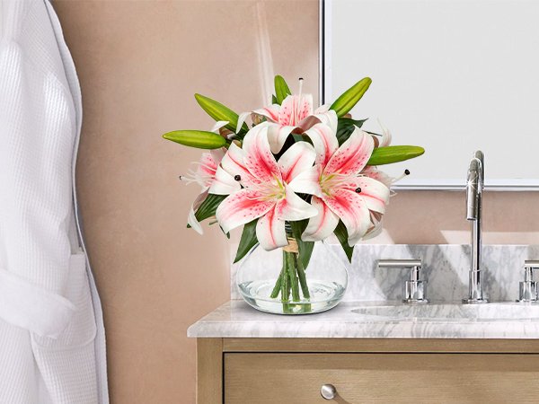 Artificial orange tiger lily arrangement with six silk flower heads in a glass vase with faux water, placed on a bathroom vanity.