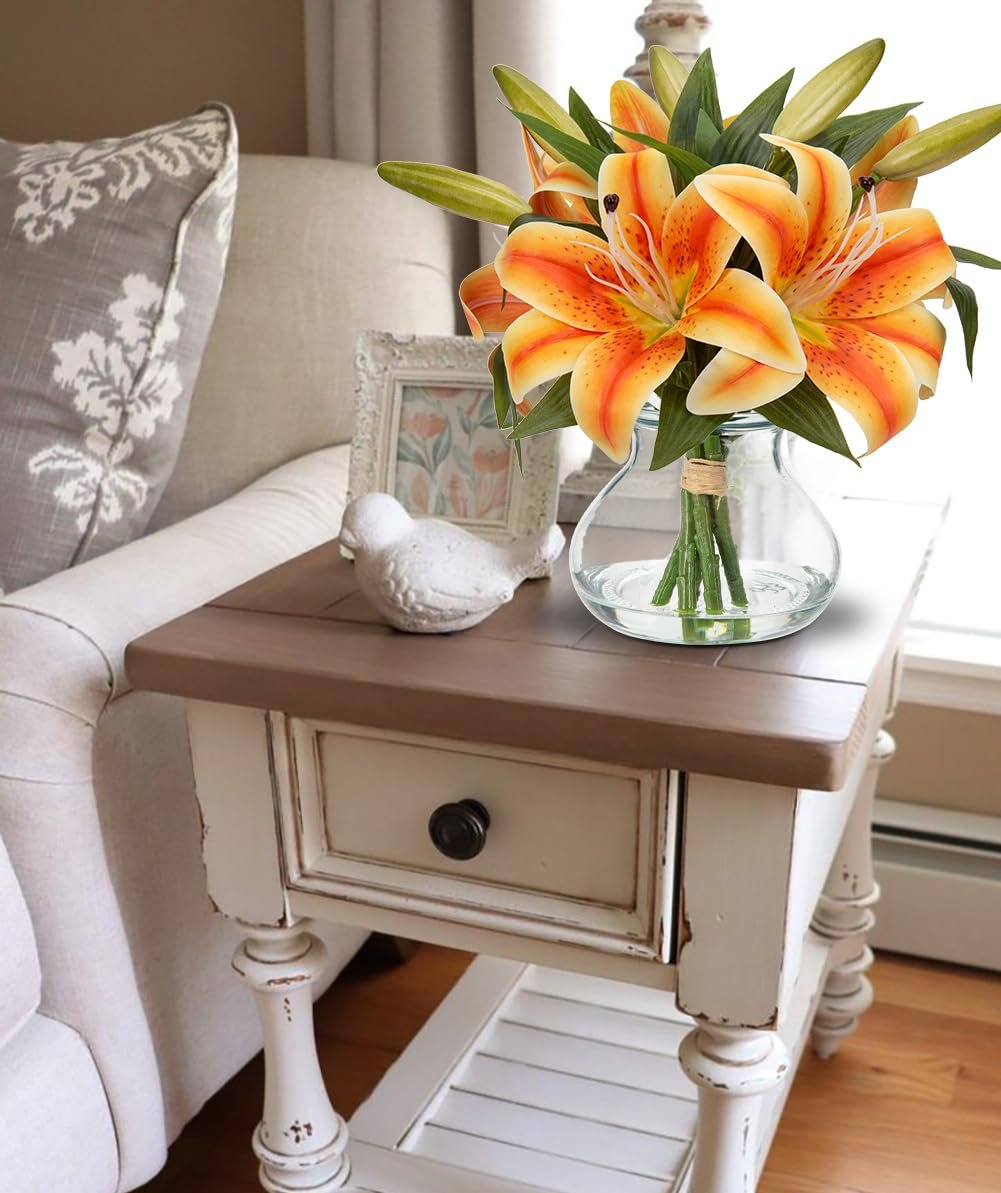Orange tiger lily artificial flower arrangement in a glass vase with faux water on a side table.