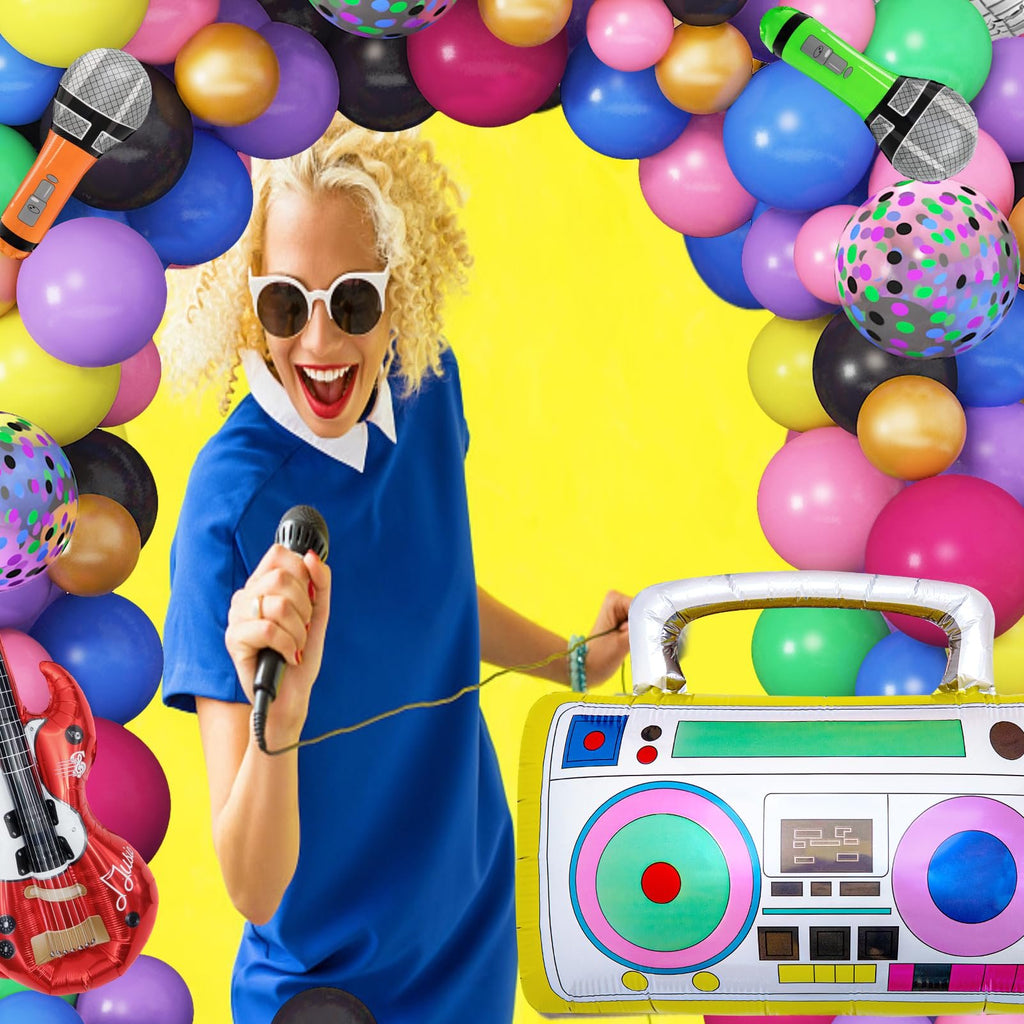 Woman singing into a microphone surrounded by colorful balloons and retro party props like a boombox and guitar