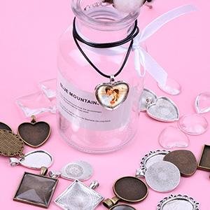 Jewelry making supplies including pendant trays, glass cabochons, and necklace cords arranged around a glass bottle.