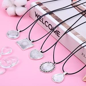 Assortment of five pendant trays with necklace cords on a pink surface, showing various shapes including round, square, heart, oval, and teardrop.