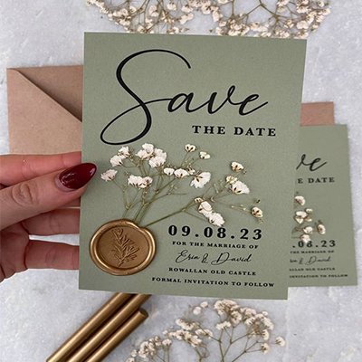 Save the Date card with dried baby's breath flowers and a gold wax seal, featuring wedding details.