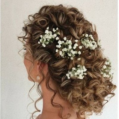 Woman's curly brown hair styled with small white baby's breath flowers