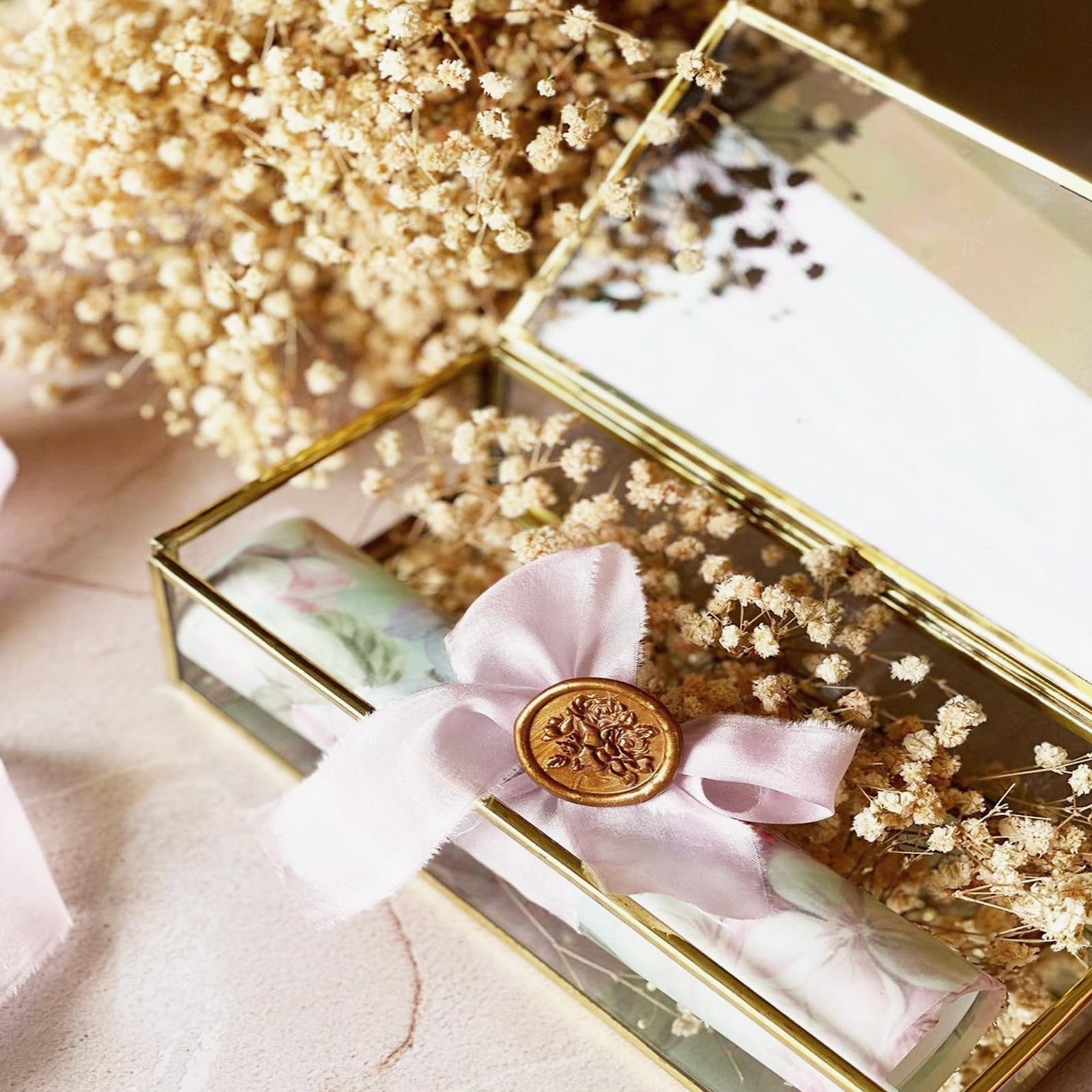 Glass box with dried baby's breath flowers and a scroll tied with pink ribbon and a wax seal.