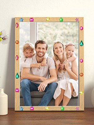 Family of four smiling behind a wooden picture frame decorated with colorful craft gems