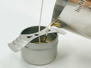 Soy candle making kit: pouring melted wax into a metal container with a wick holder and wick.
