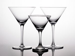 Three clear martini glasses of varying sizes on a reflective surface against a white background.