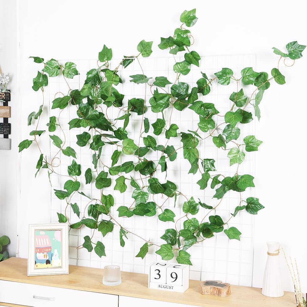 Artificial grape ivy vine garland draped on a white grid wall, with decorative items on a shelf below.