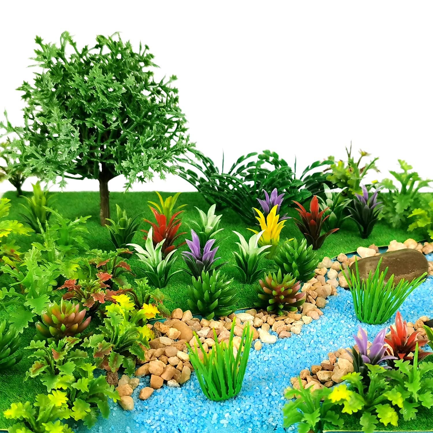 Assortment of miniature artificial trees and plants arranged in a diorama with blue gravel river and rocks