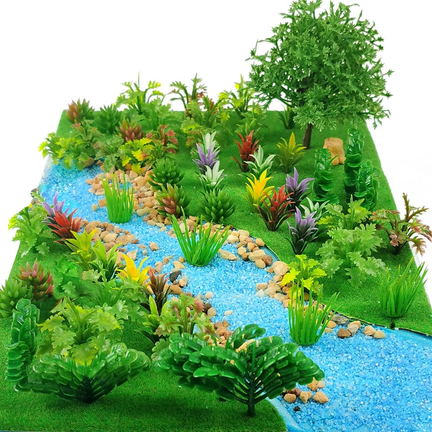 Miniature model landscape with a blue river, green grass, and various colorful plants and trees.