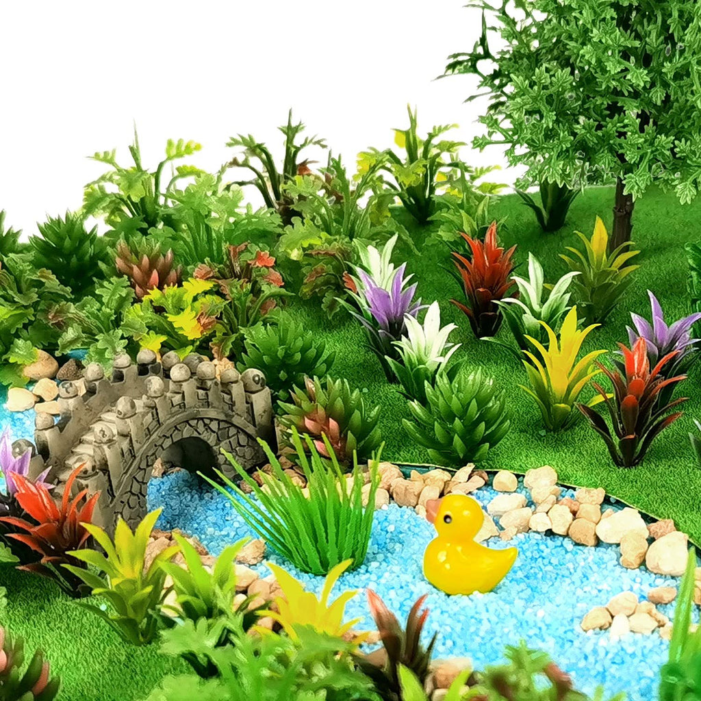 Miniature garden scene with a stone bridge over a blue gravel stream, a yellow duck, and various colorful artificial plants.