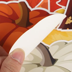 Close-up of a hand peeling a fall-themed bulletin board cutout featuring pumpkins and maple leaves.