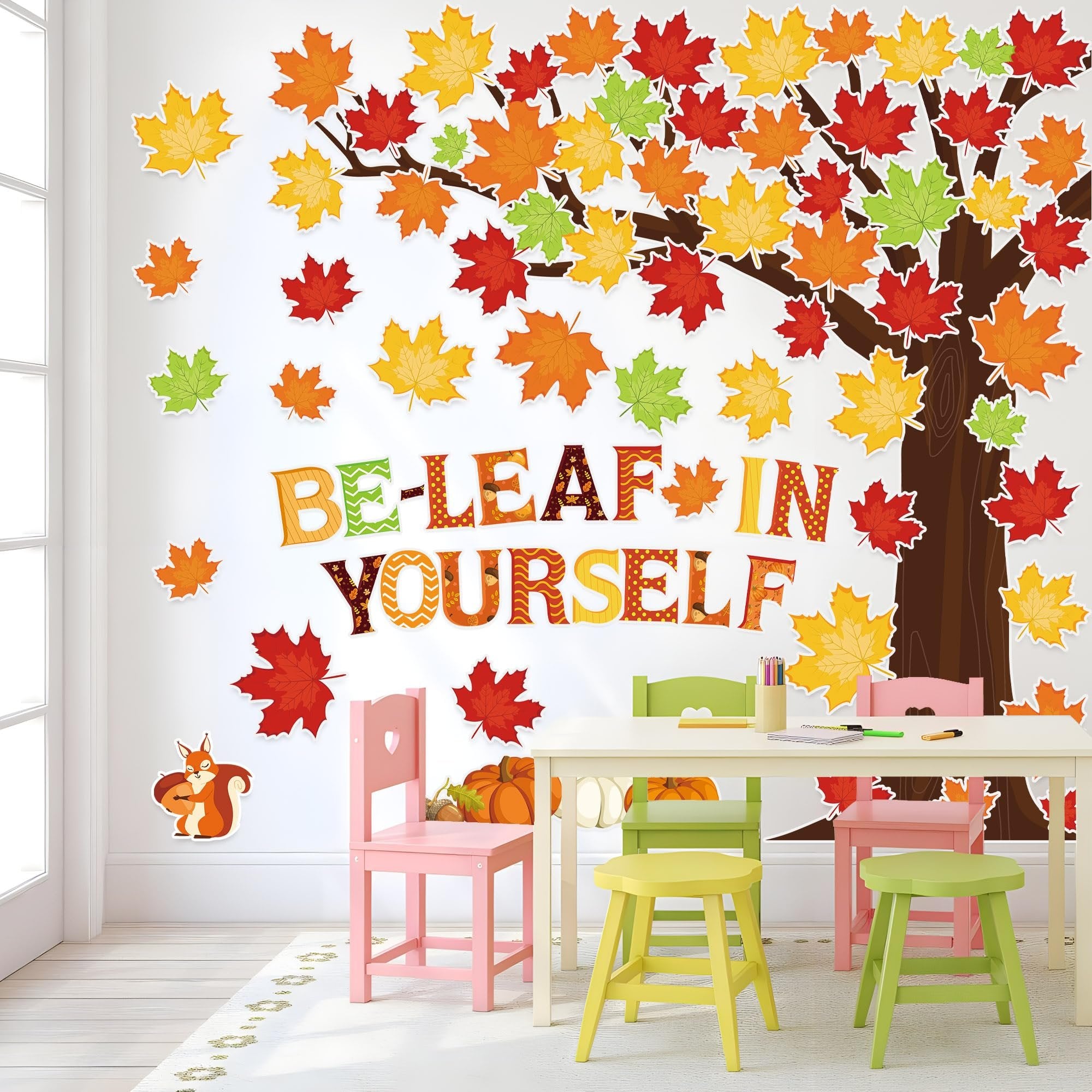 Fall bulletin board cutouts with a tree, maple leaves, pumpkins, and the phrase "BE-LEAF IN YOURSELF" displayed in a classroom setting.