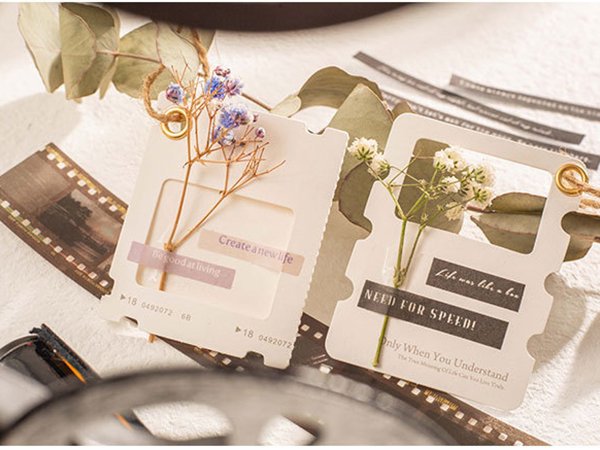 Scrapbook paper kit with decorative film strips, cards, and dried flowers, arranged artistically.
