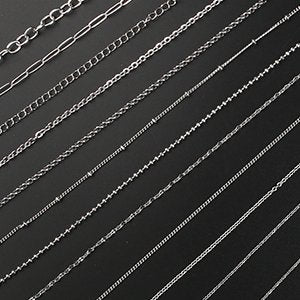 Collection of 12 different styles of silver-tone stainless steel jewelry chains laid out diagonally on a dark background.