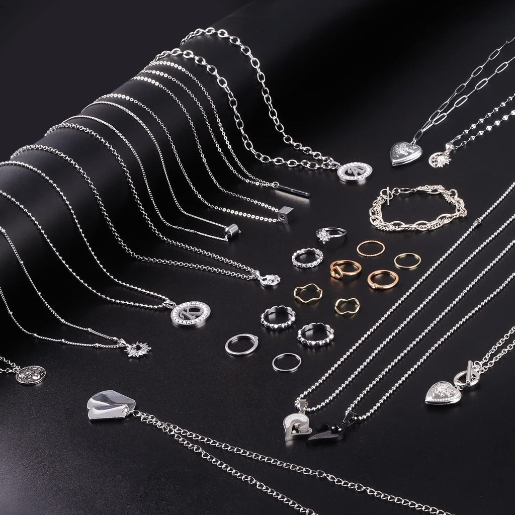 Assortment of silver and gold-tone necklaces, bracelets, and rings laid out on a black background.