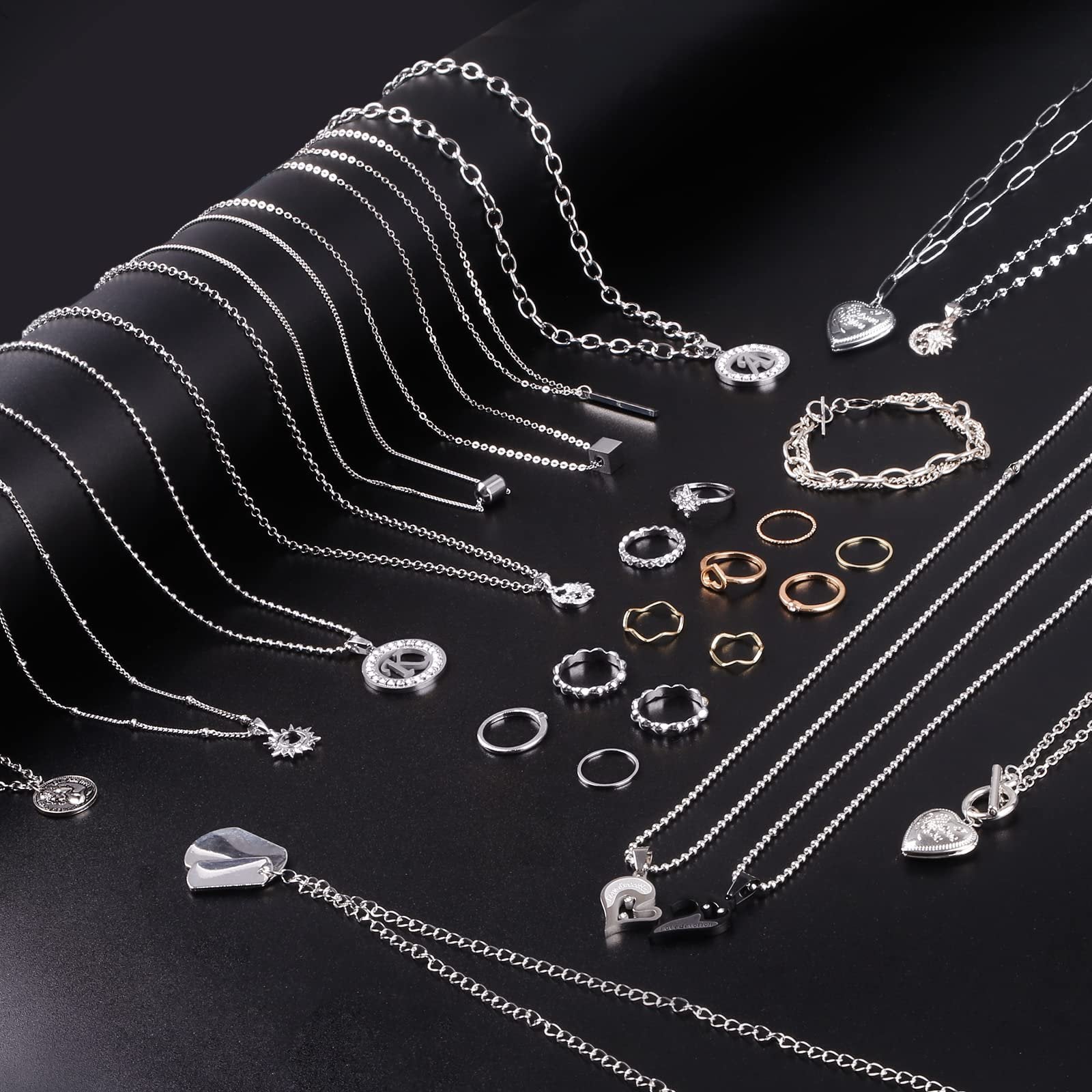 Assortment of silver and gold-tone necklaces, bracelets, and rings laid out on a black background.