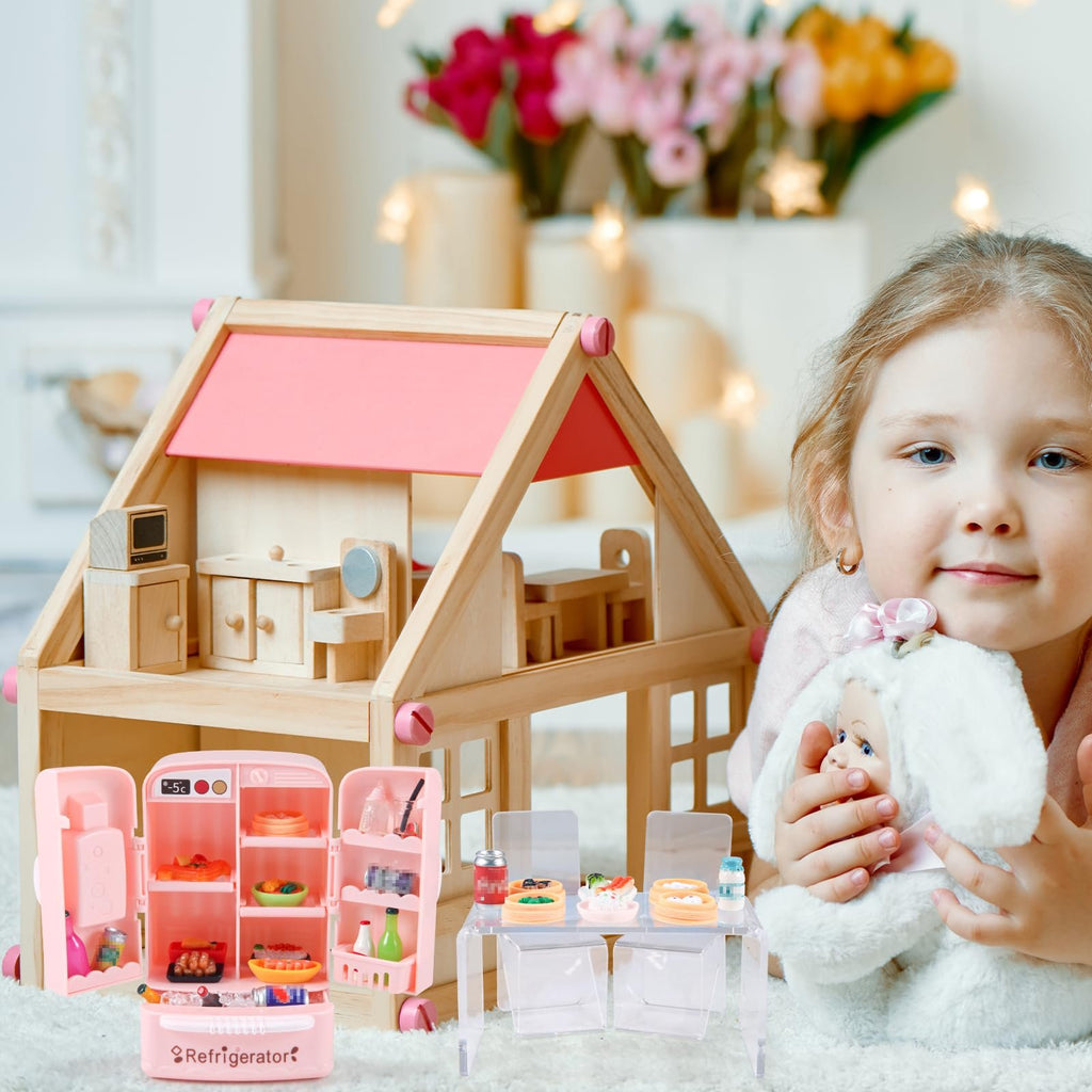 Young girl holding a doll next to a wooden dollhouse and a pink toy refrigerator with miniature food.