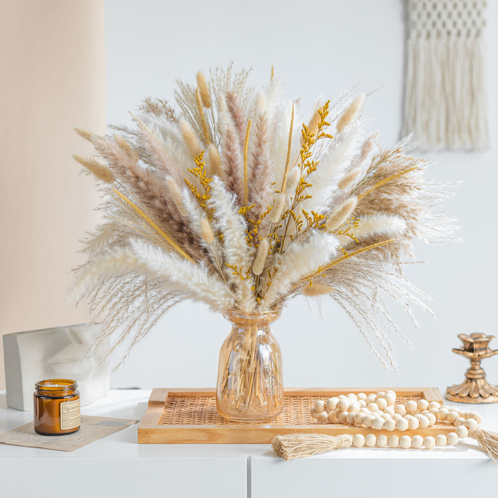 Boho dried pampas grass bouquet in amber vase with decorative beads and candle on white surface