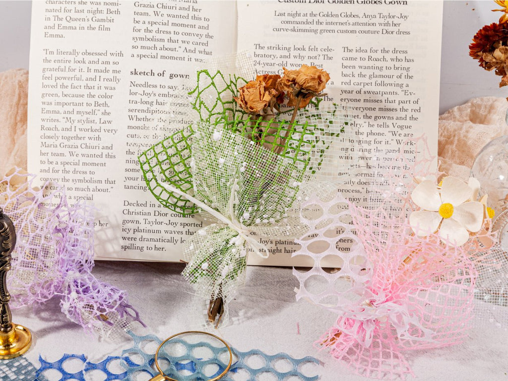 Collage of textured scrapbook paper and mesh fabric in pastel colors, arranged on open books with dried flowers and decorative elements.