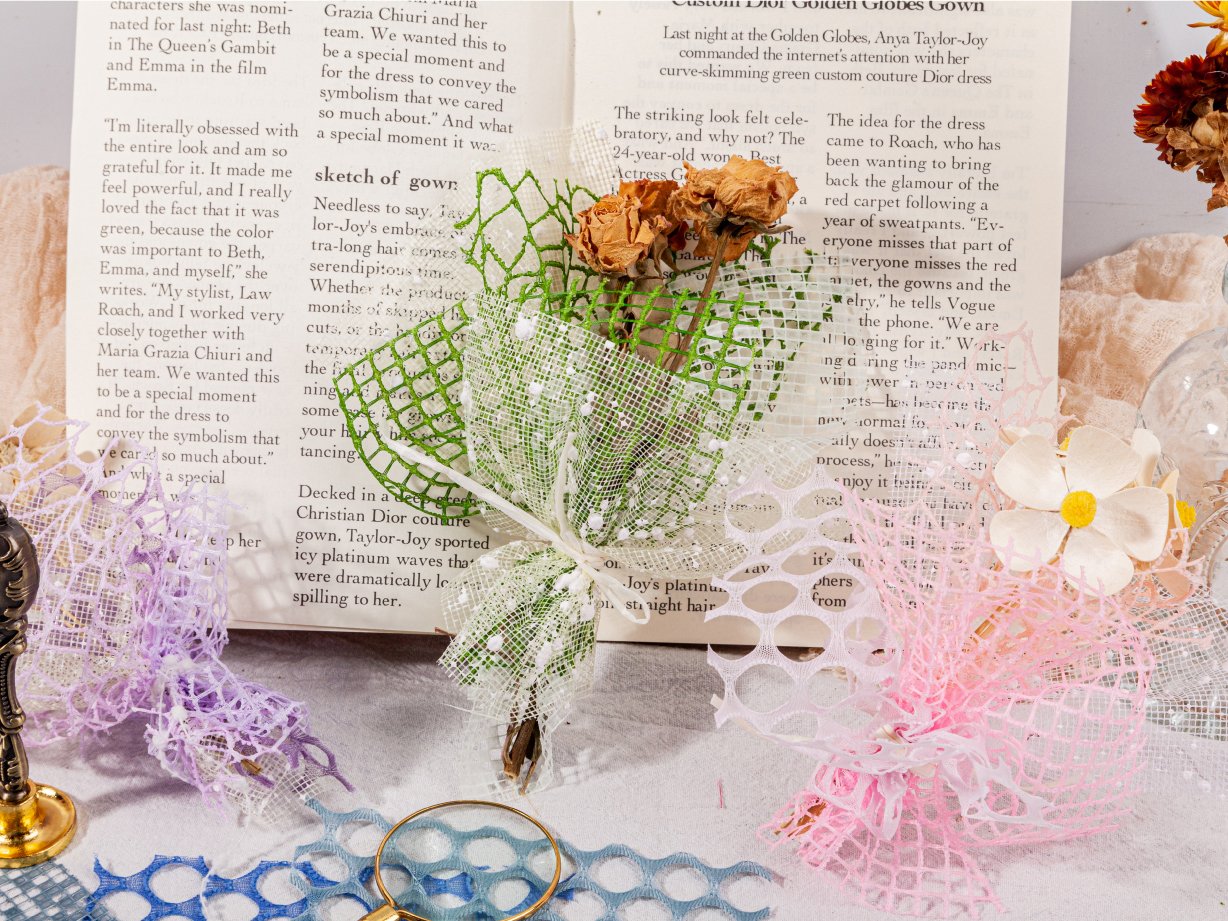 Collage of textured scrapbook paper and mesh fabric in pastel colors, arranged on open books with dried flowers and decorative elements.