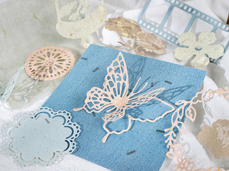 Assortment of decorative paper cutouts including a butterfly, flowers, and film strip elements on a blue cardstock.