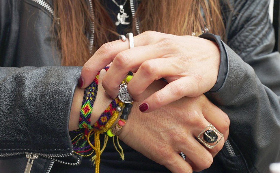 Close-up of hands wearing friendship bracelets and rings, one hand adjusting a bracelet.